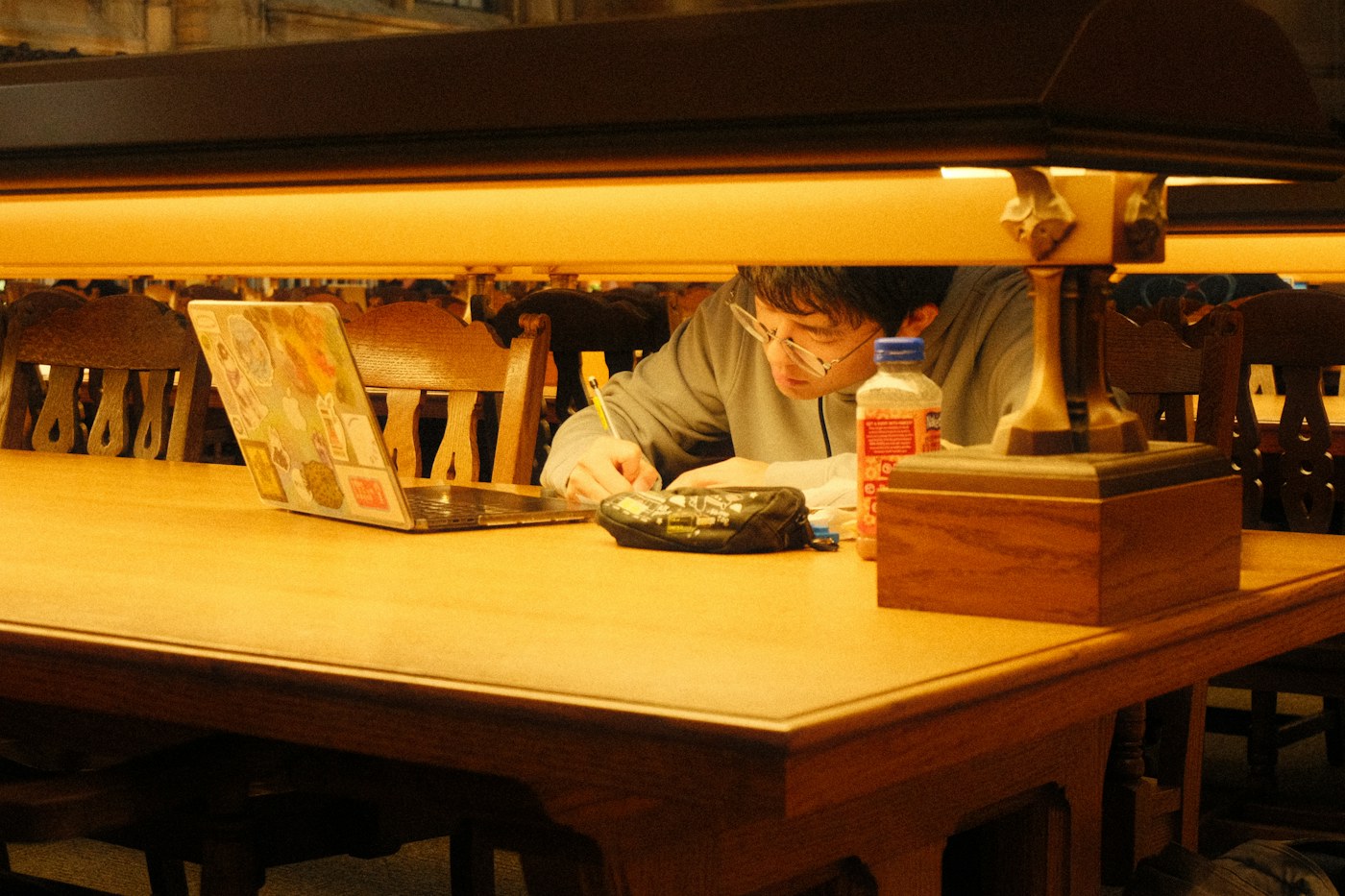 Student concentrating on handwritten notes beside a laptop in a library